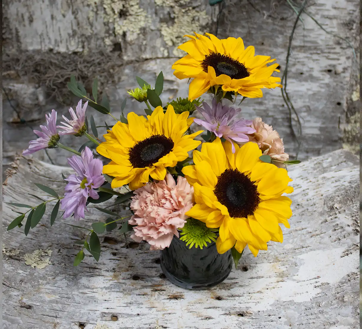 This charming arrangement combines the vibrant beauty of golden sunflowers with the cheerful simplicity of daisies and the soft, ruffled petals of pastel carnations.
