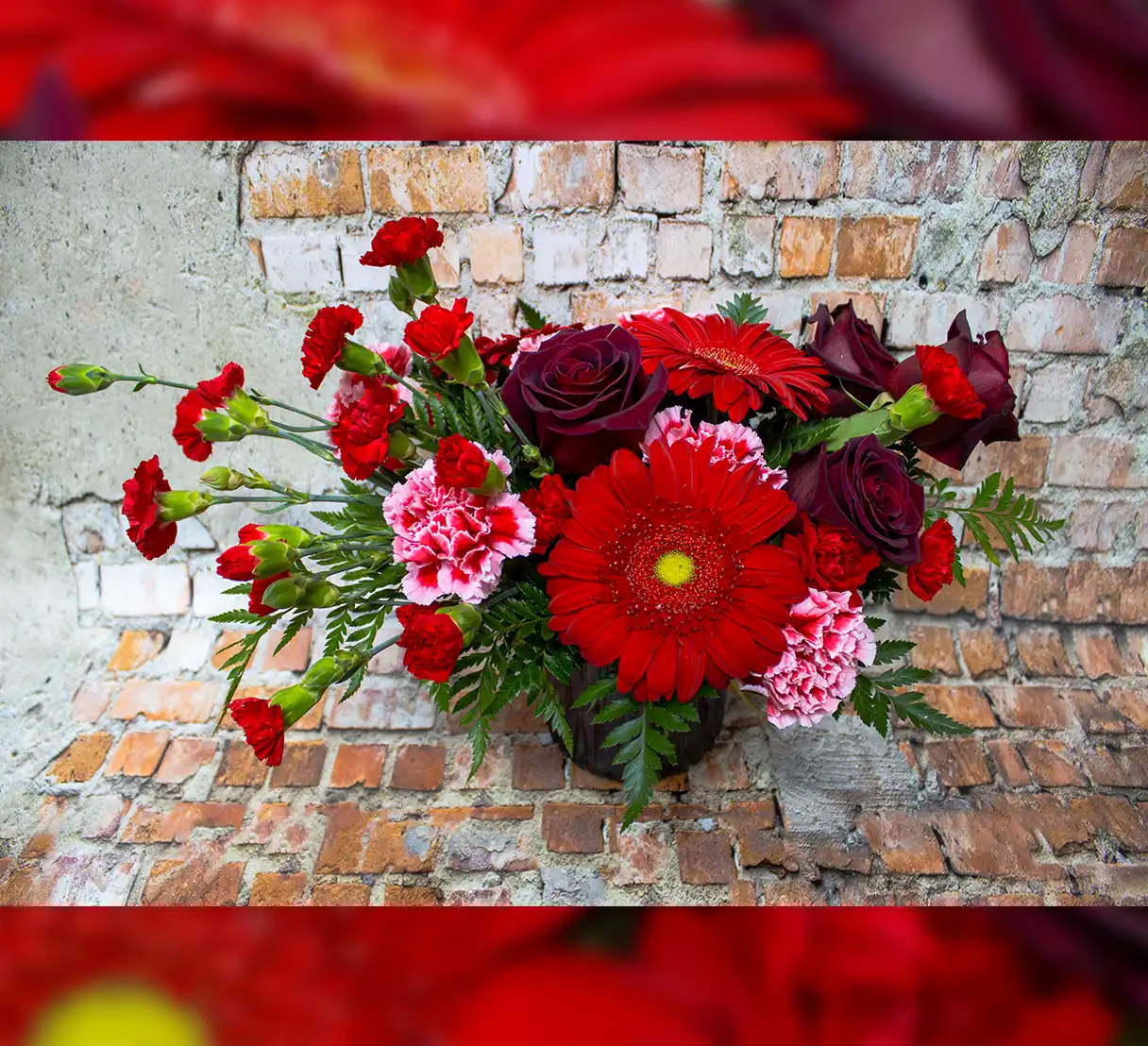 This striking bouquet features a passionate blend of red Gerber daisies, roses, and mini carnations, artfully arranged in a bold red glass vase. The Gerber daisies bring a cheerful, radiant charm, while the classic roses evoke timeless elegance and romance. The mini carnations add a delicate texture with their petite, ruffled blooms, enhancing the bouquet's lush appearance. The red glass vase amplifies the vibrant hues of the flowers, creating a cohesive and dramatic statement piece that exudes warmth and love.